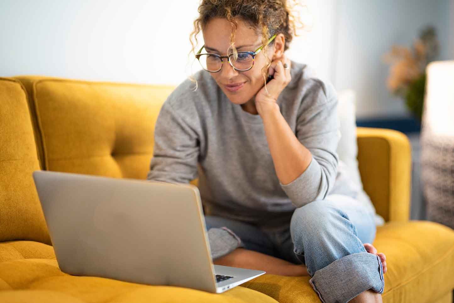 Female sitting on a yellow couch using laptop and smiling
